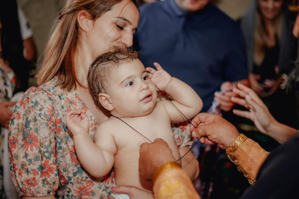 A mother lovingly holds her baby during a family celebration, surrounded by loved ones exchanging gifts.